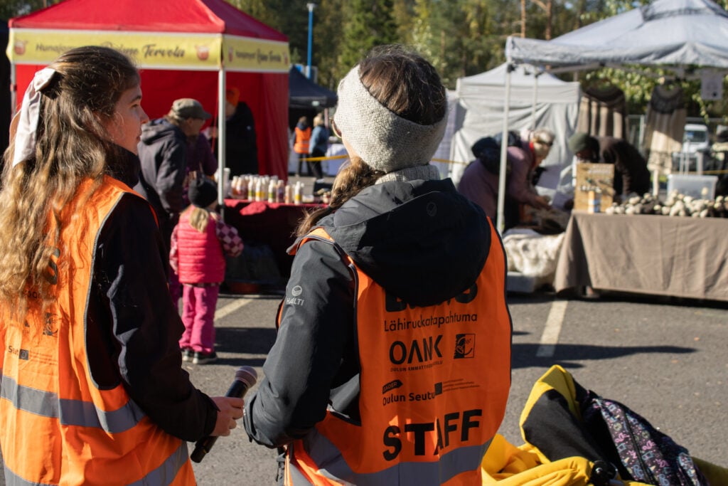 Tori tapahtuma, työntekijät oransseissa liiveissä keskustelemassa.