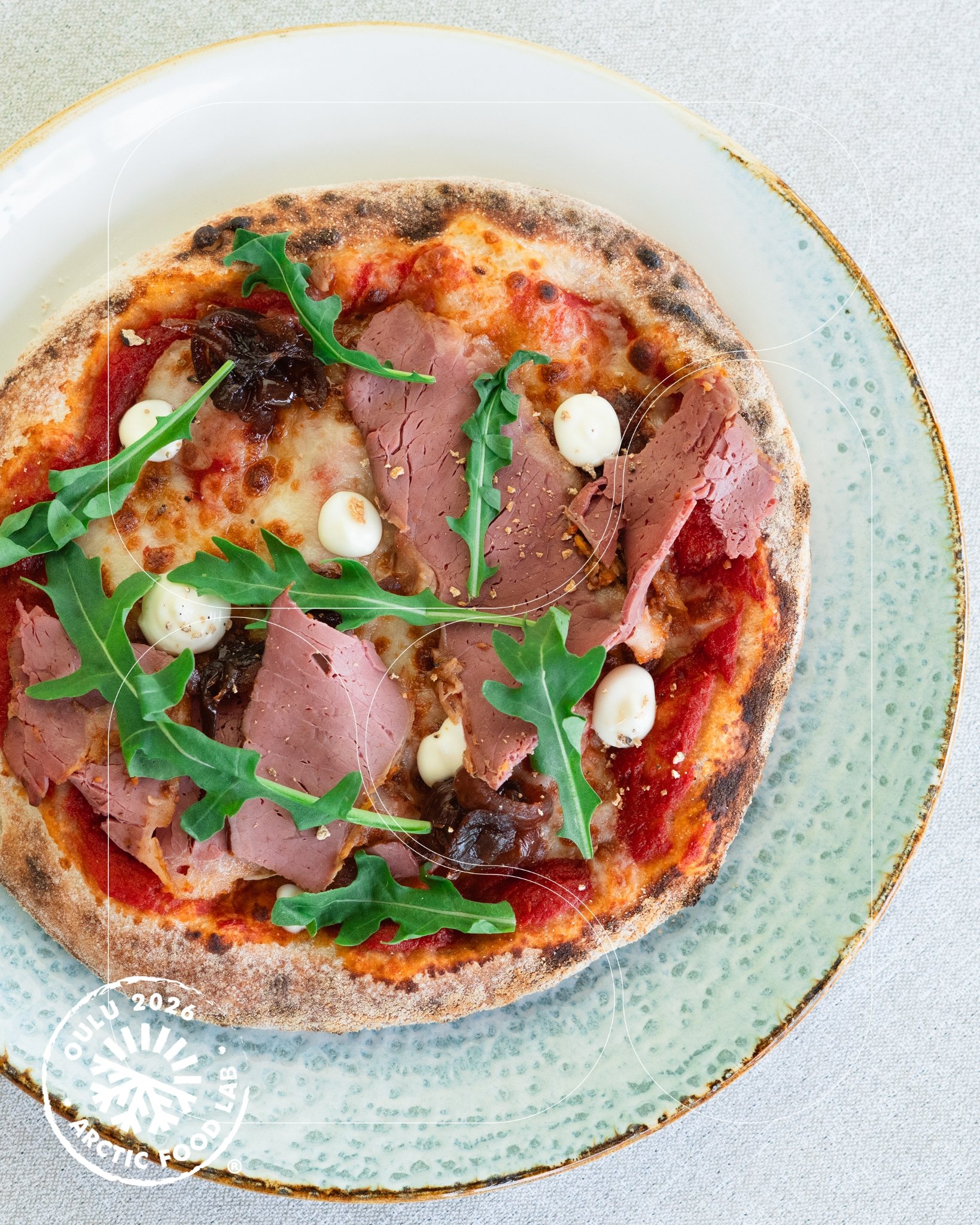 Pizza ilmakuivatulla kinkulla ja rucolalla lautasella.