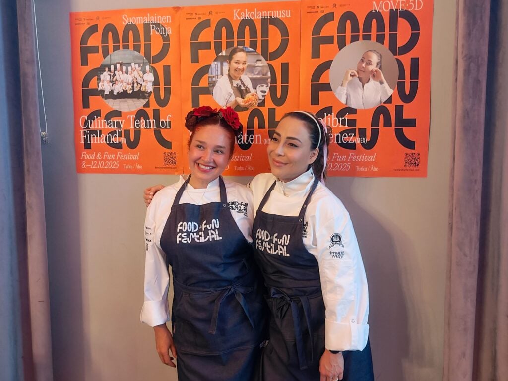 Kaksi kokkia seisoo seinän edessä.