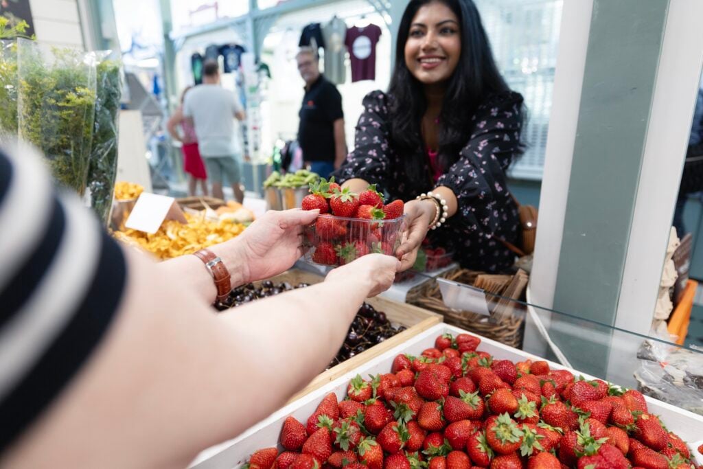 Kädet ojentavat mansikoita toiselle ihmiselle.